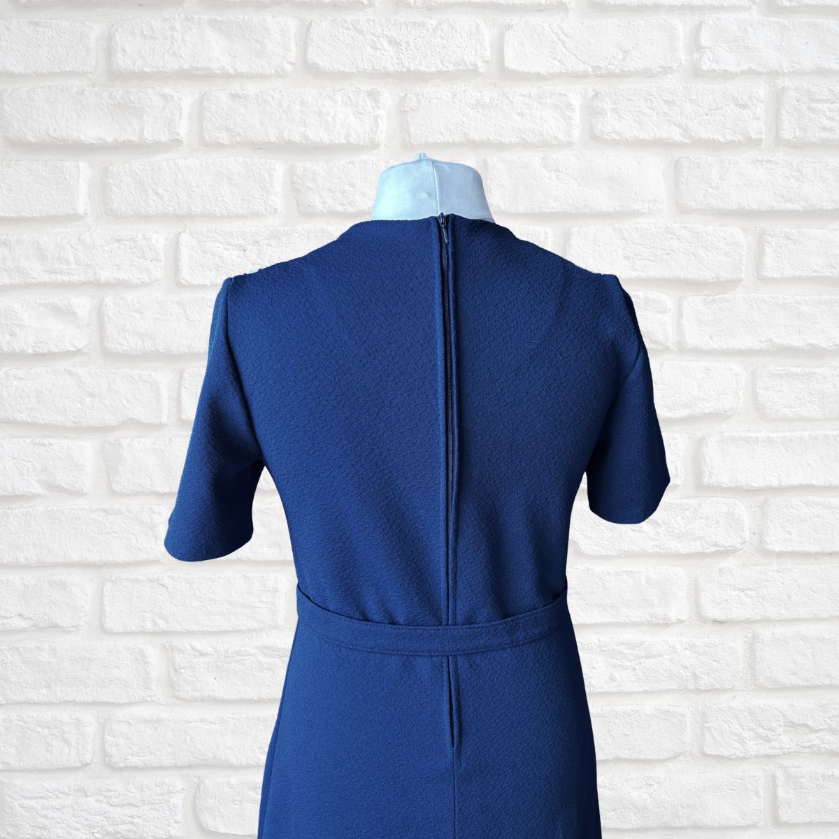 Blue dress on a mannequin against a white brick wall background