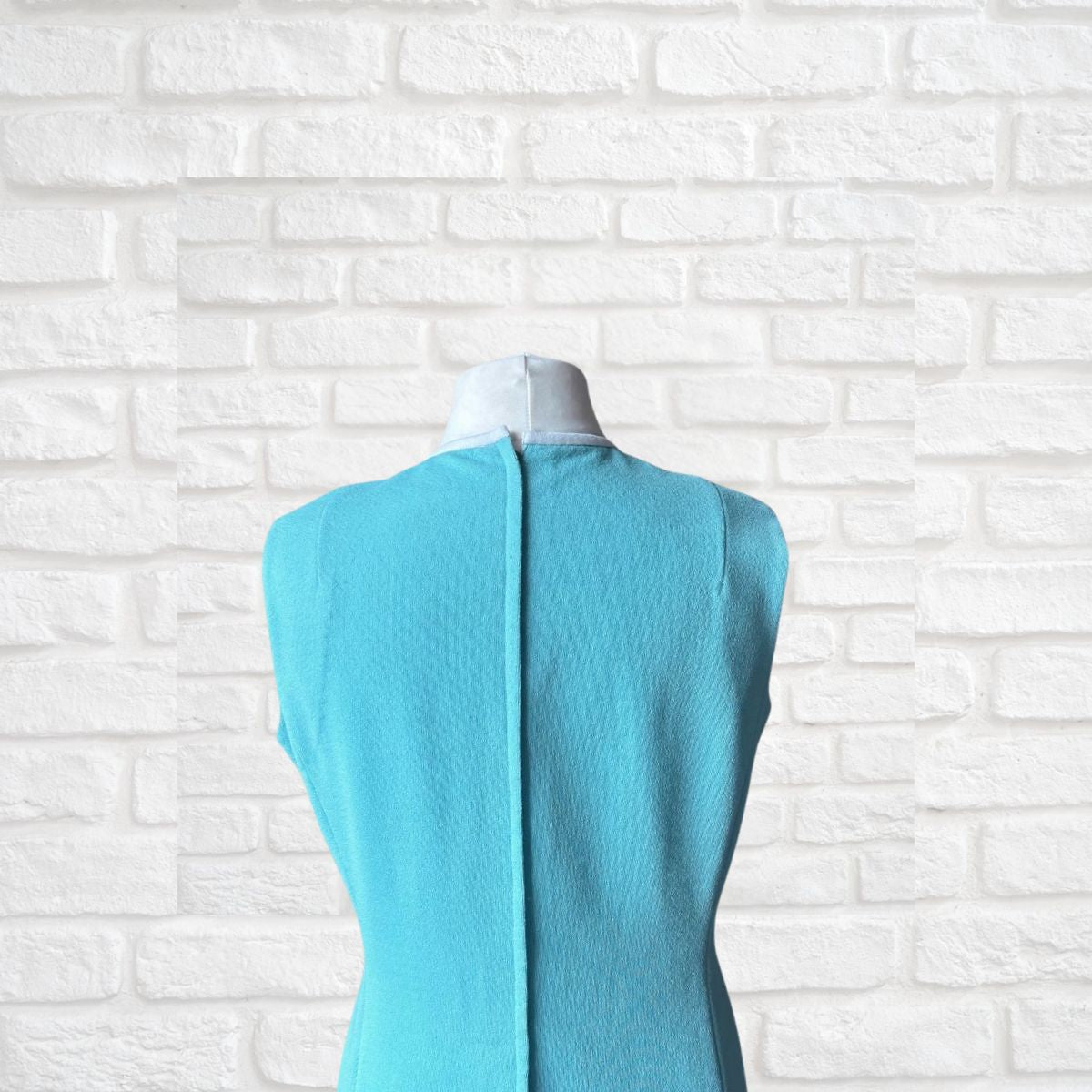 Turquoise dress  on a mannequin against a white brick wall background