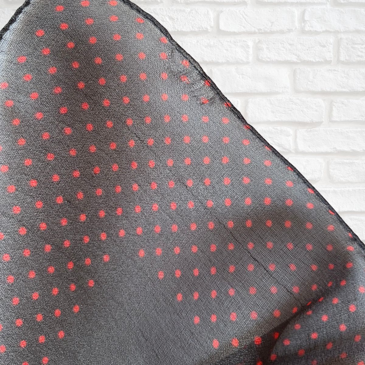 Black scarf with red polka dots on a white brick wall background