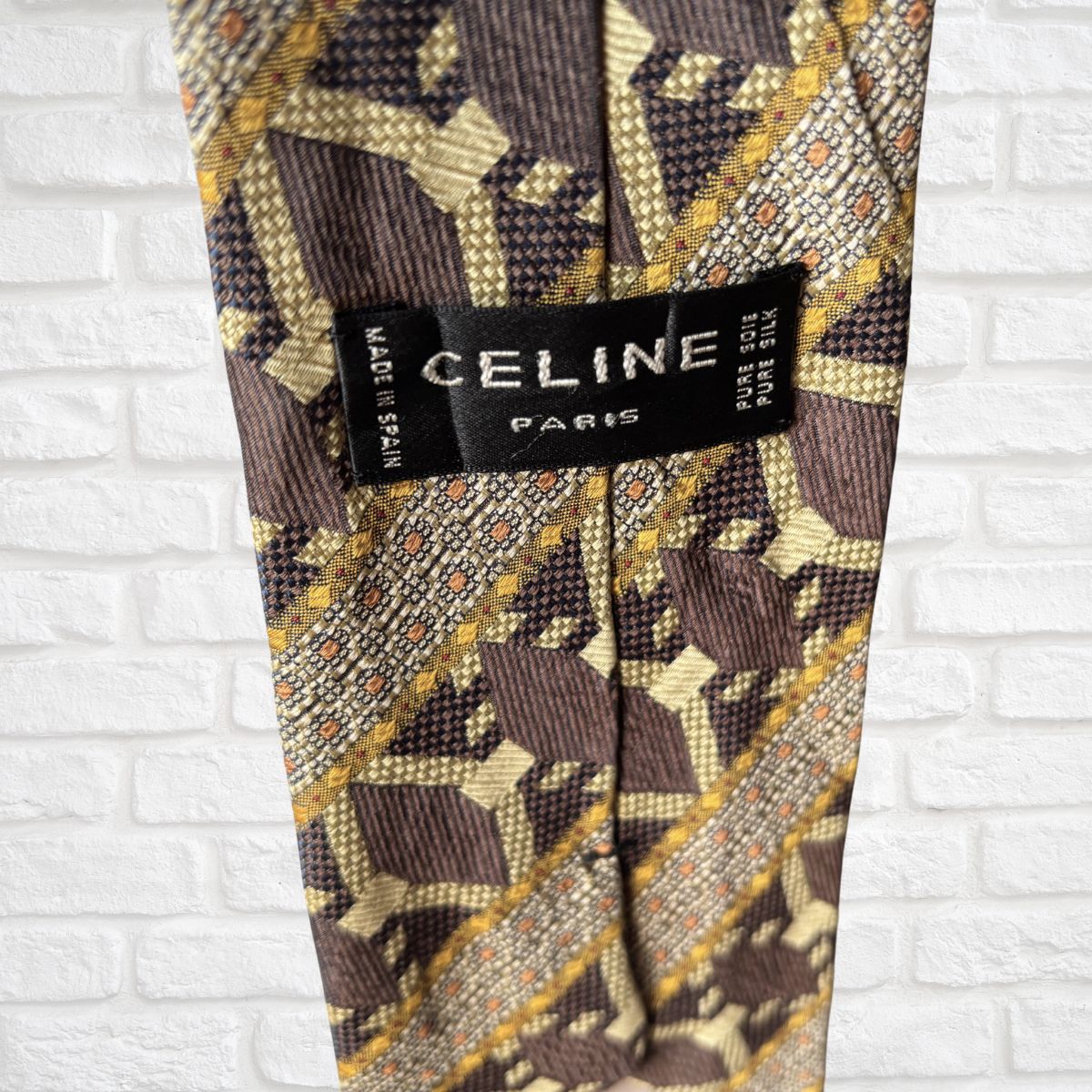 Patterned vintage tie with a Celine label against a white brick wall background