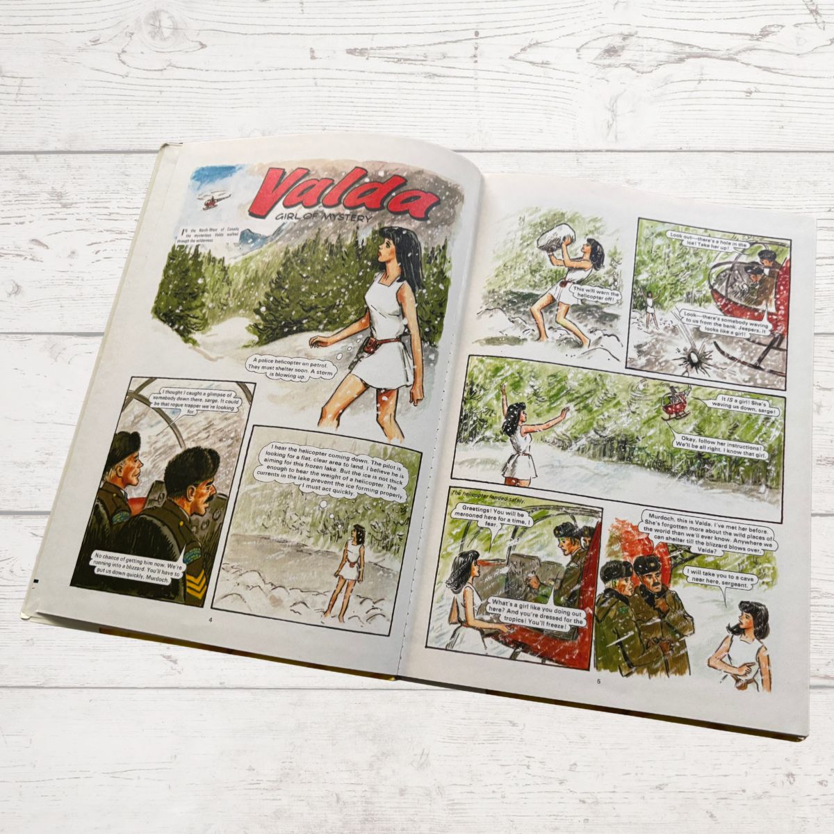 Comic book open to a page with illustrations and text on a wooden surface