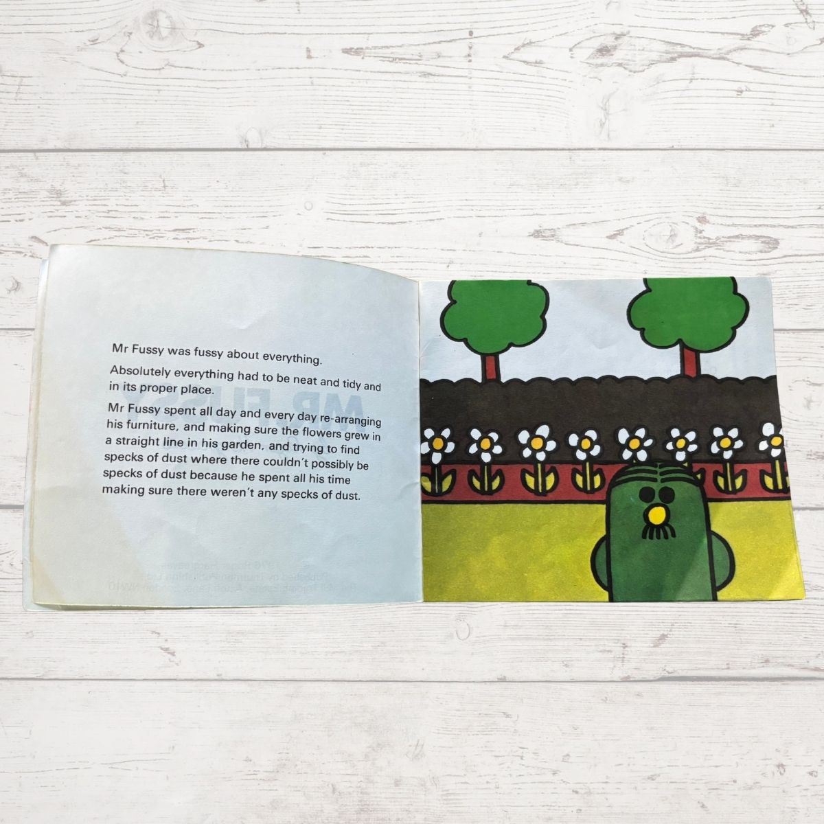 Open book with a cartoon character with a very neat garden  and text on a wooden surface