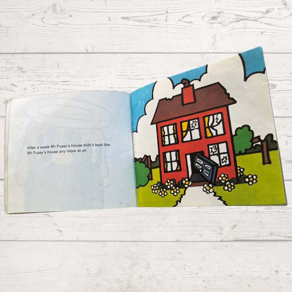 Open book with a colorful illustration of a house with broken windows on a wooden surface