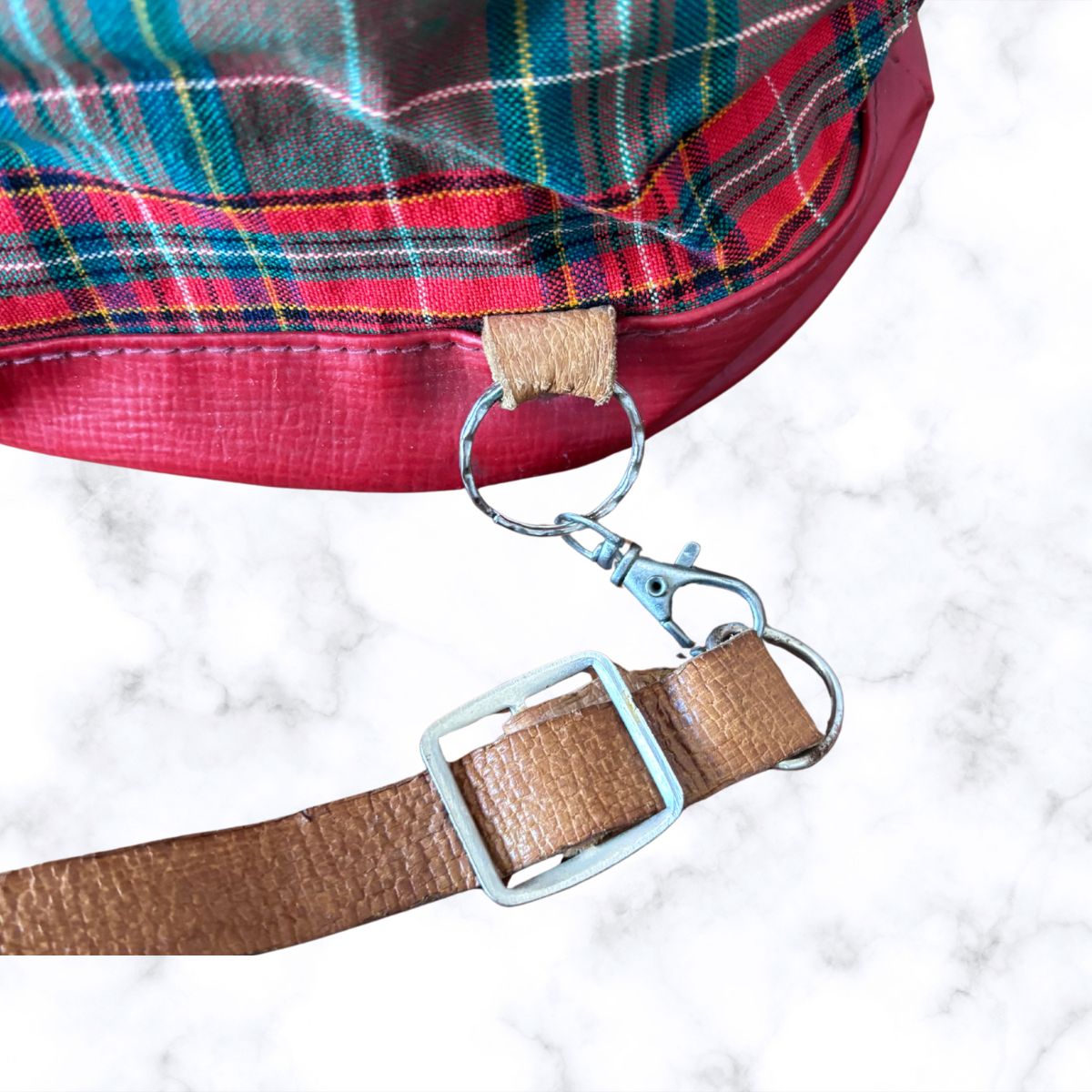 Close-up of a plaid bag with a brown strap and metal buckle on a white background