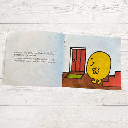 Mr Happy next to a red door at the bottom of a staircase 