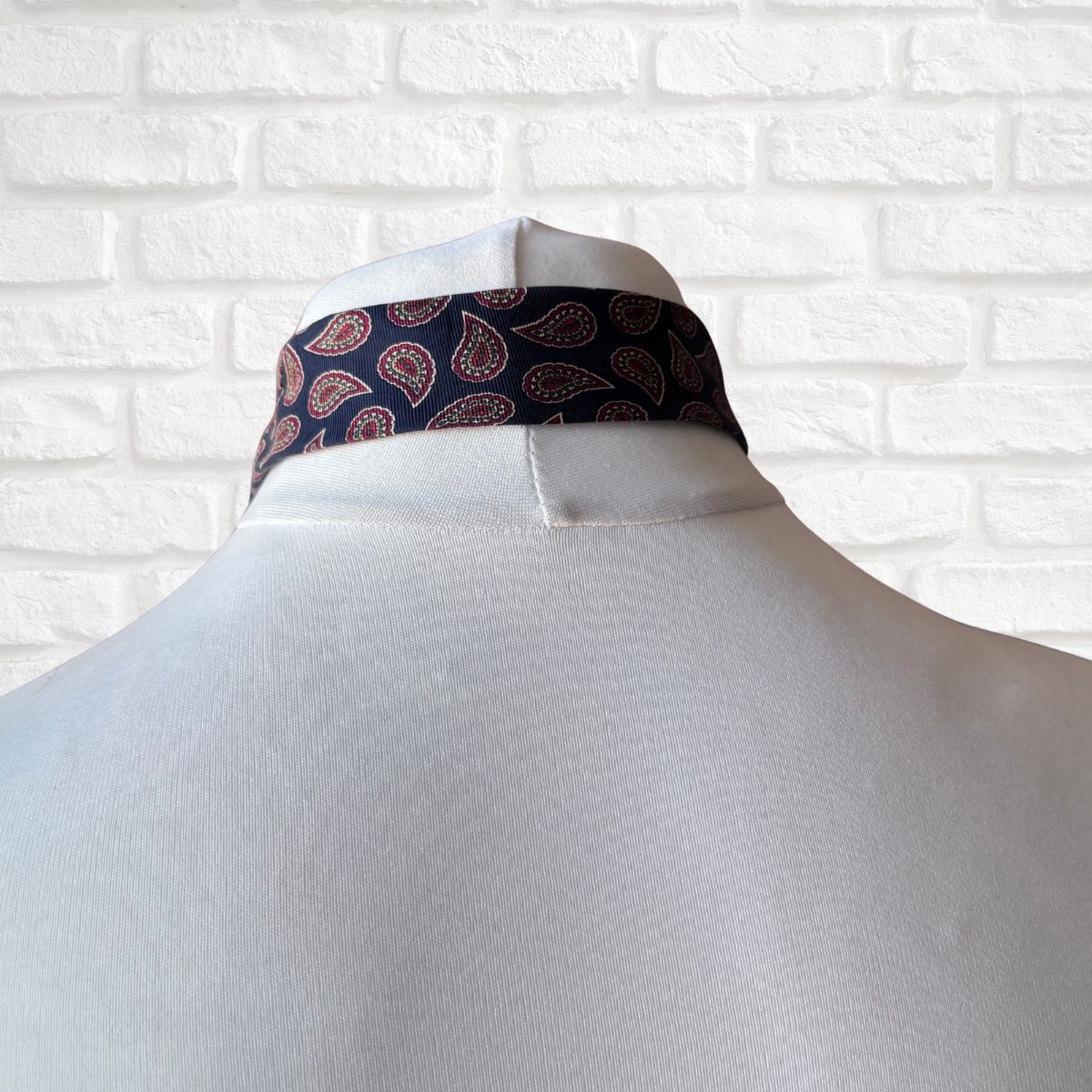 Navy blue paisley-patterned tie on a mannequin against a white brick wall.