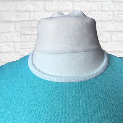 White collar on a turquoise dress against a white brick wall background