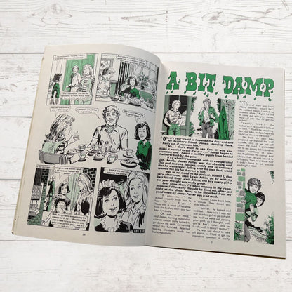 Comic book open to a page with illustrations and text on a wooden surface