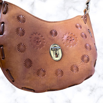 Tooled leather shoulder bag with gold hardware on a white background 
