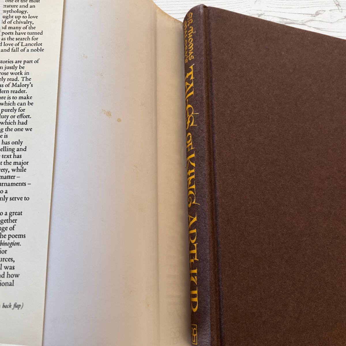 Close-up of an open book with a brown hardcover on a light wooden surface.