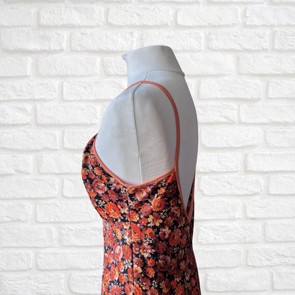 Mannequin wearing a floral dress with orange straps against a white brick wall.