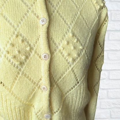 Light yellow  knitted cardigan with button details on a white brick wall background
