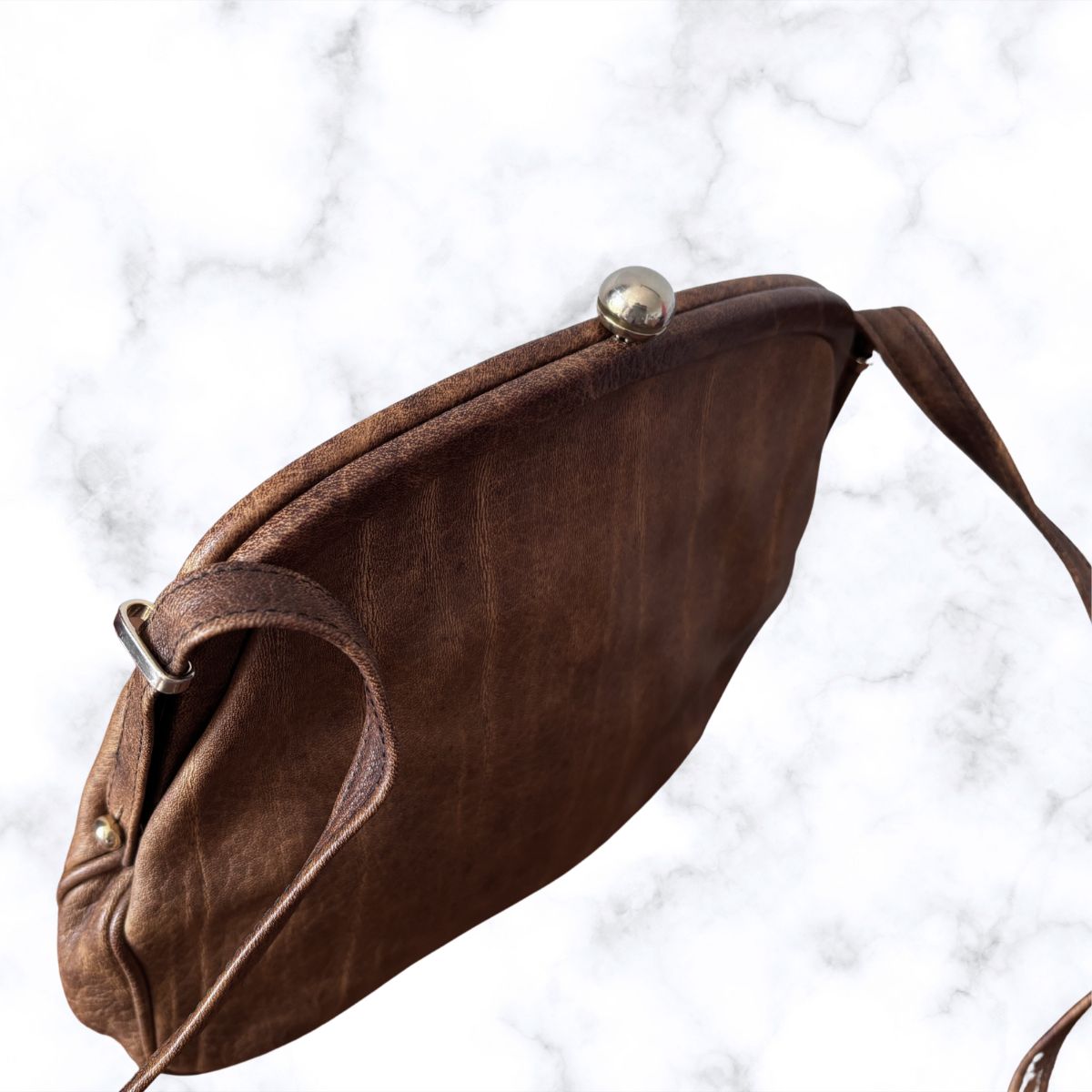 Brown leather look handbag with gold accents on a white marble background