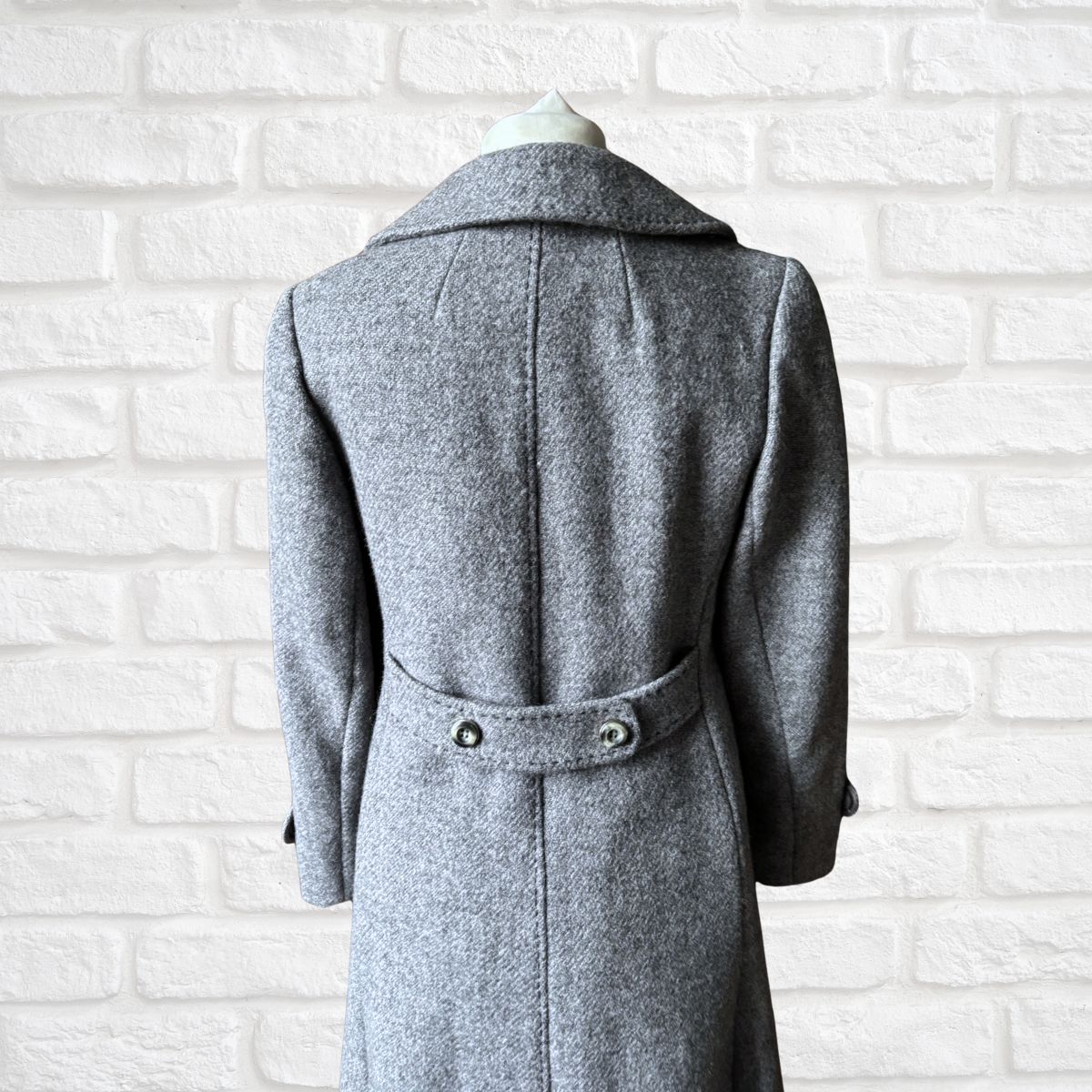 Gray coat on a mannequin against a white brick wall