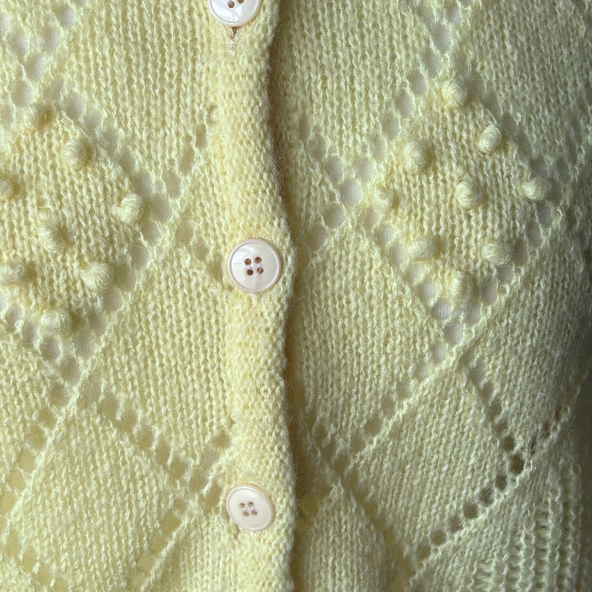 Close-up of a light yellow  knitted cardigan with button details