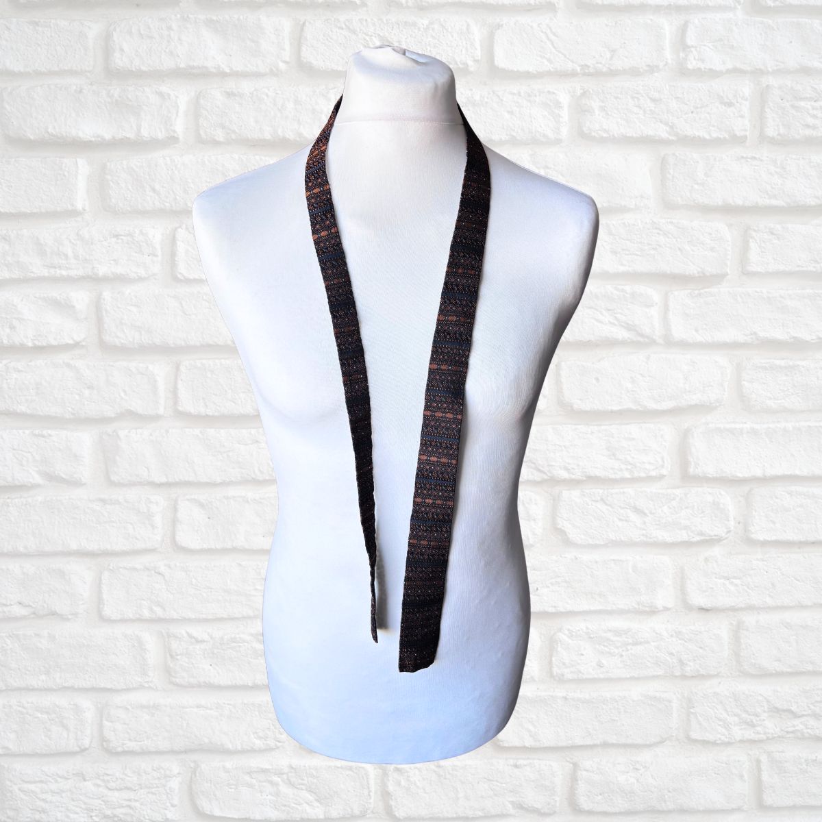 Mannequin wearing a skinny tie against a white brick wall background