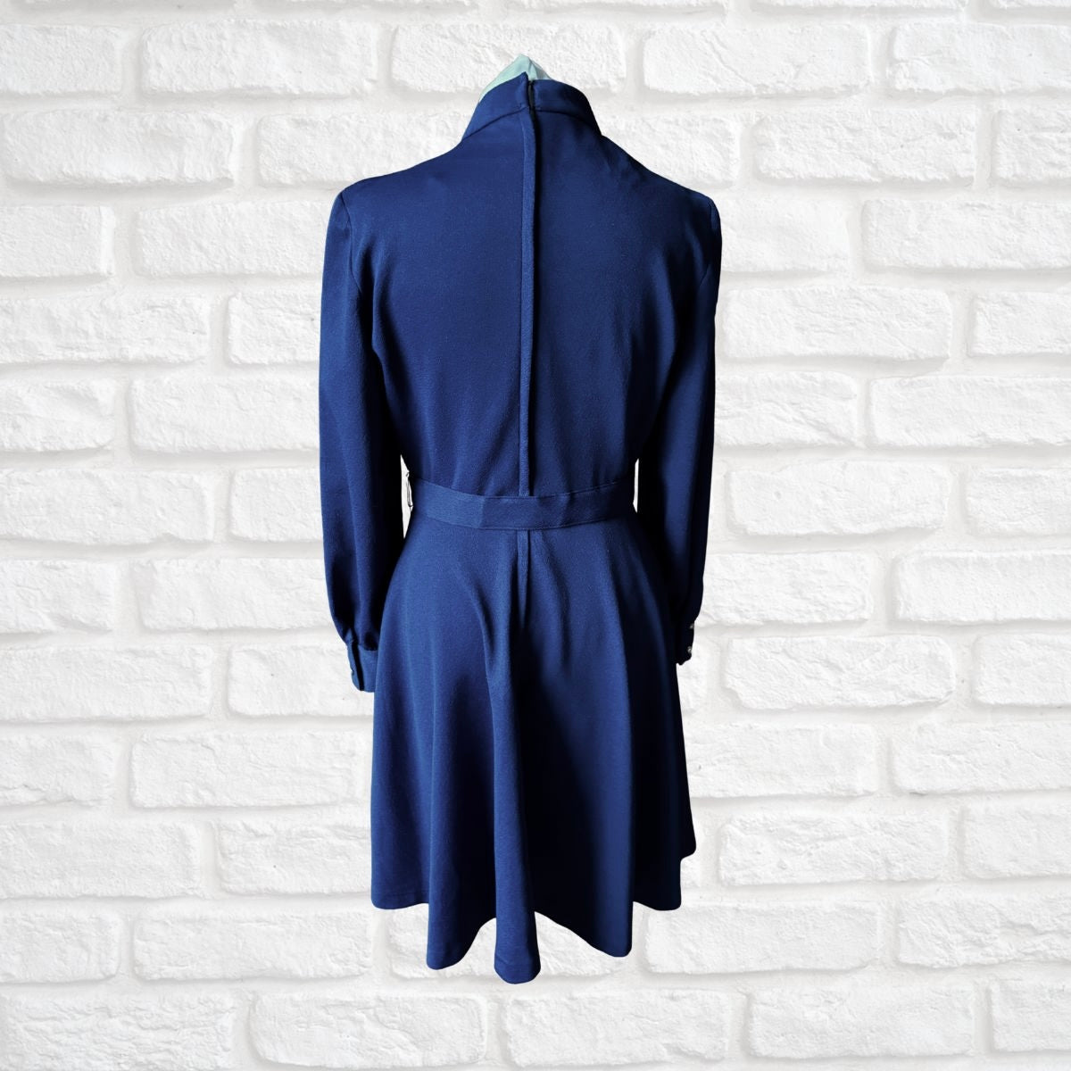 Blue dress on a hanger against a white brick wall