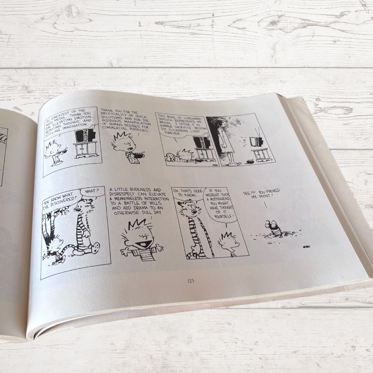 Open book with black and white comic strip on a light wooden surface