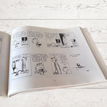 Open book with black and white comic strip on a light wooden surface