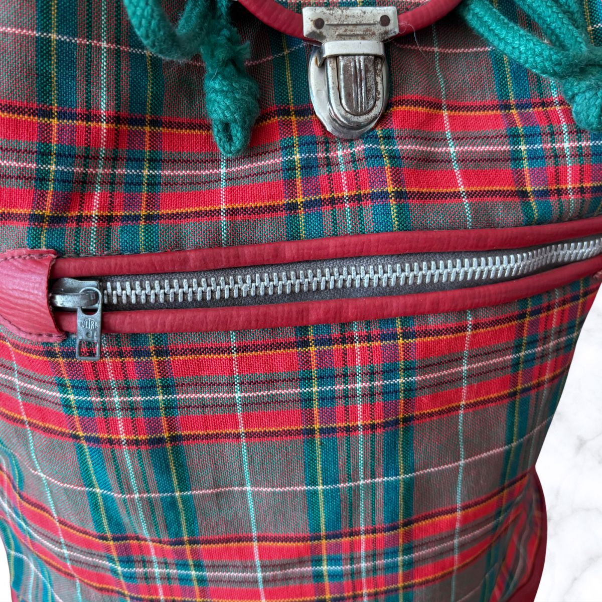 Close-up of a plaid bag with a zipper, showing red, green, and gray colors.