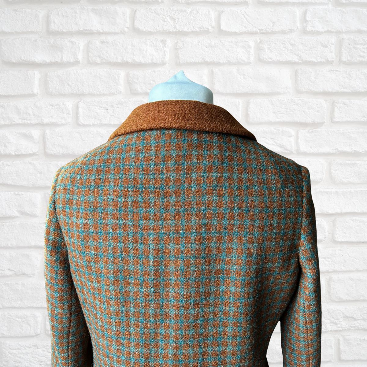 Houndstooth patterned coat on a mannequin against a white brick wall.