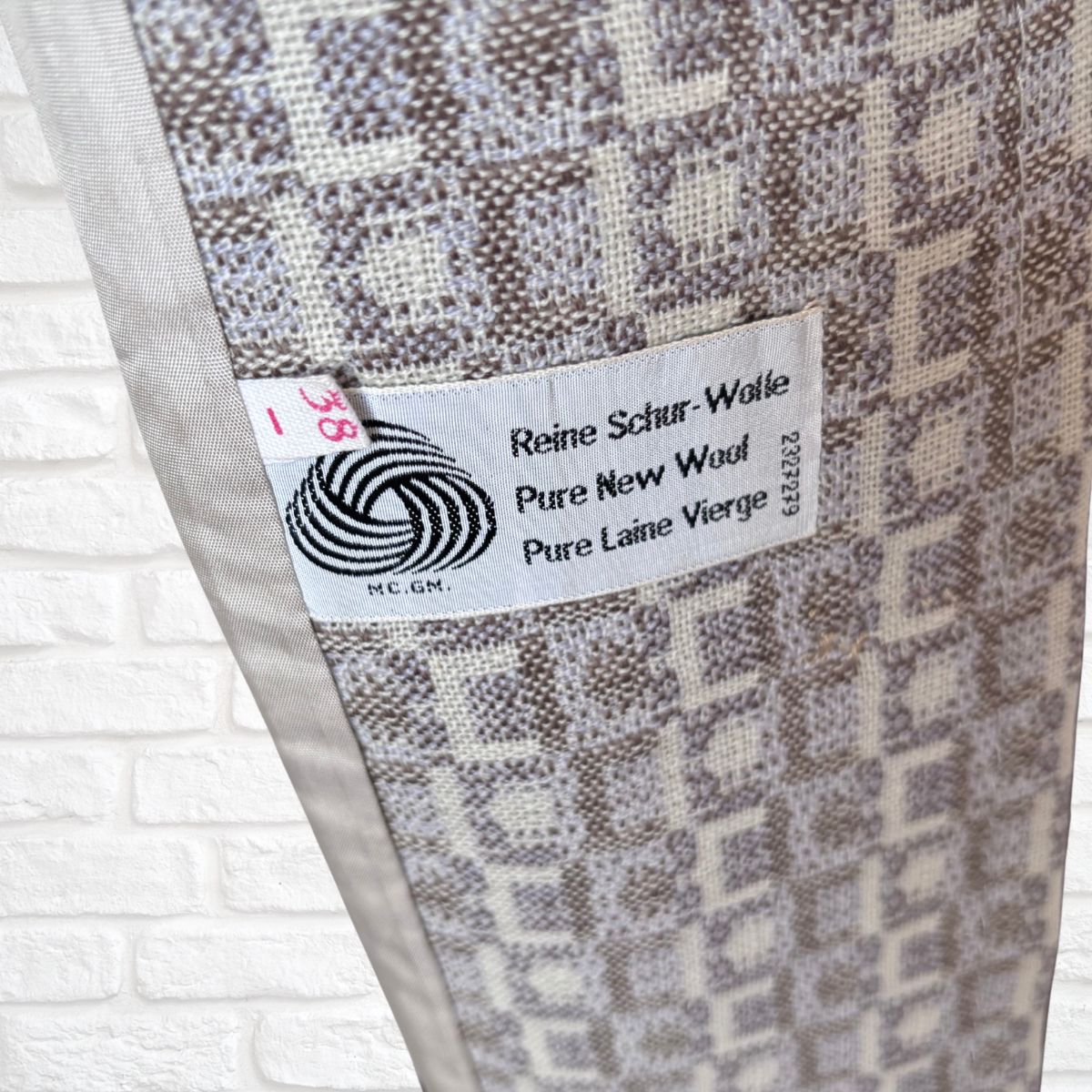 Coat with a label indicating 'Reine Schur-Wolle Pure New Wool' on a white brick background.