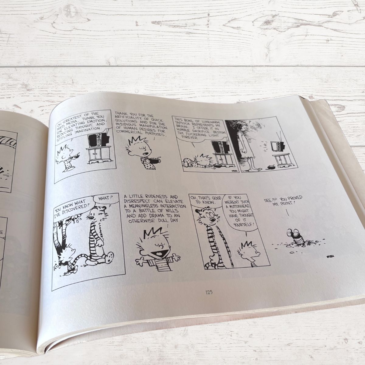 Open book with black and white comic strip on a light wooden surface