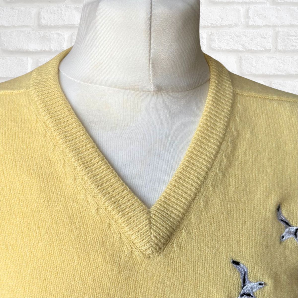 Yellow sweater with bird designs on a mannequin against a white brick wall.