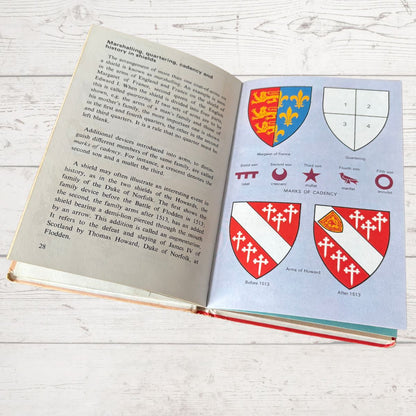 Open book on a wooden surface with illustrations of coats of arms