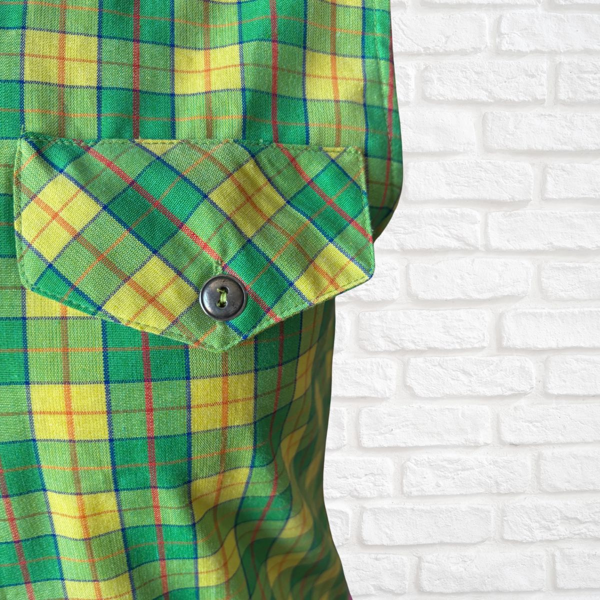 Green and yellow plaid shirt against a white brick wall