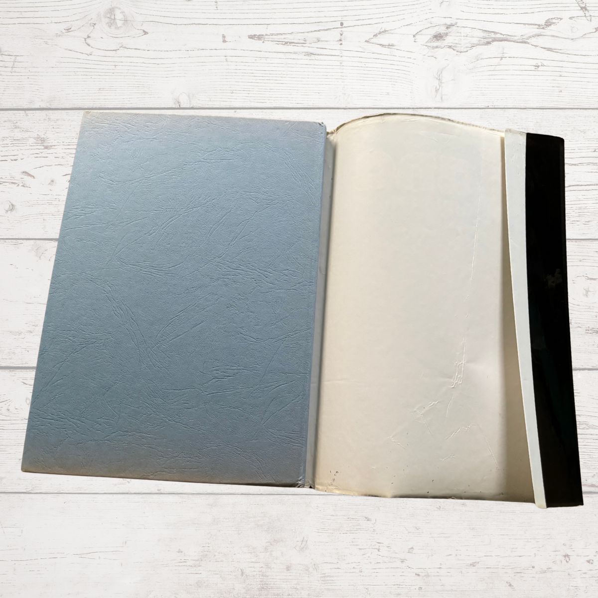 Open book with textured blue cover and white pages on a light wooden surface