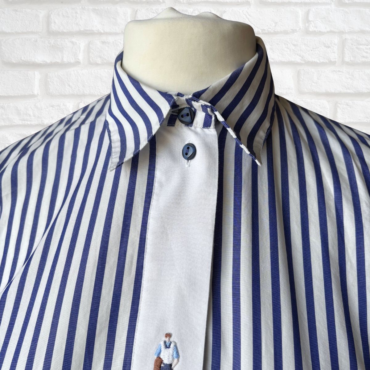 Blue and white striped shirt on a mannequin against a white brick wall.