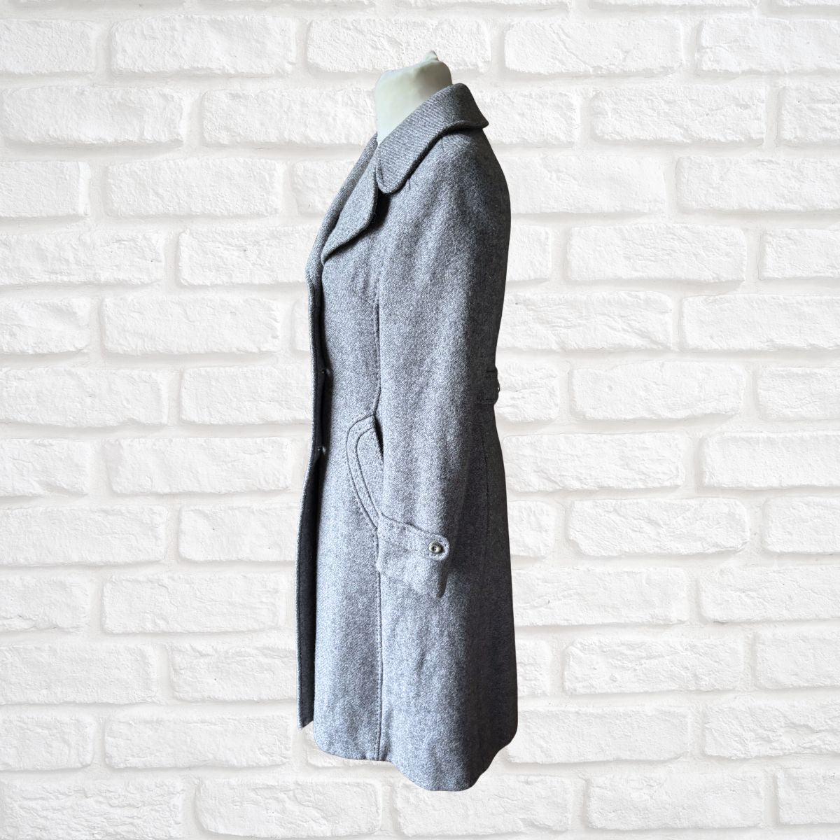 Gray coat on a mannequin against a white brick wall background