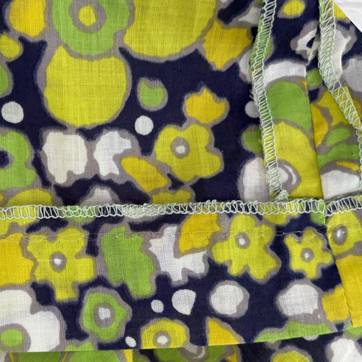Floral patterned fabric with yellow, green, and white flowers on a dark blue background.