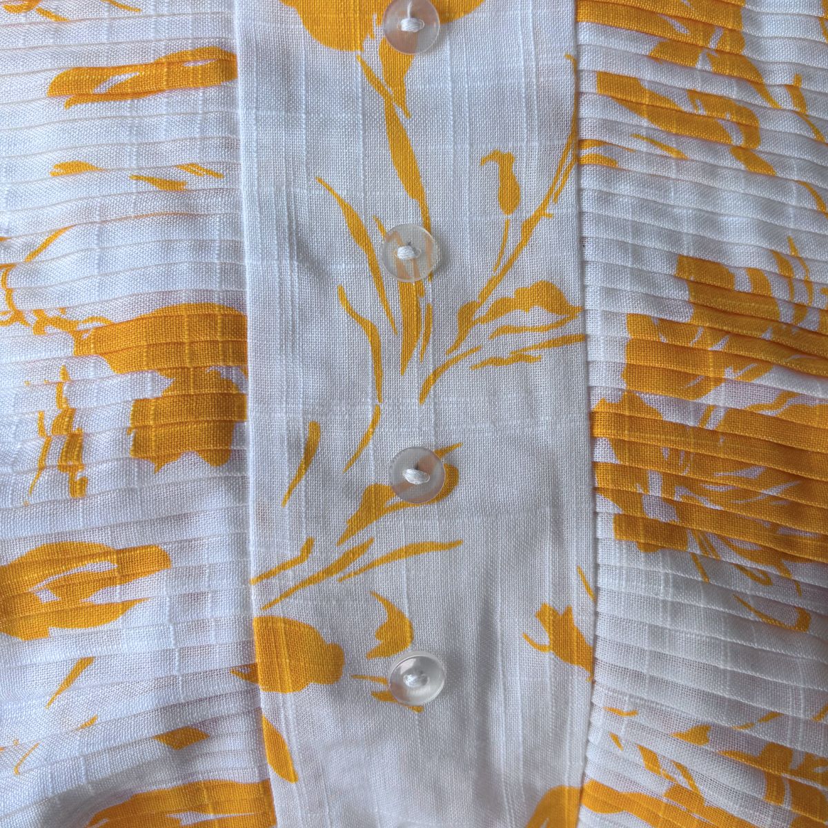 Close-up of a white dress bodice with yellow floral patterns and buttons.