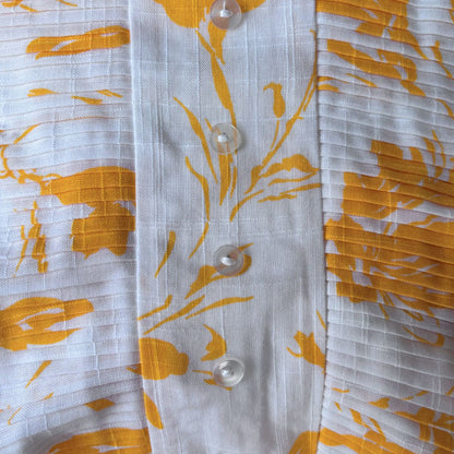 Close-up of a white dress bodice with yellow floral patterns and buttons.