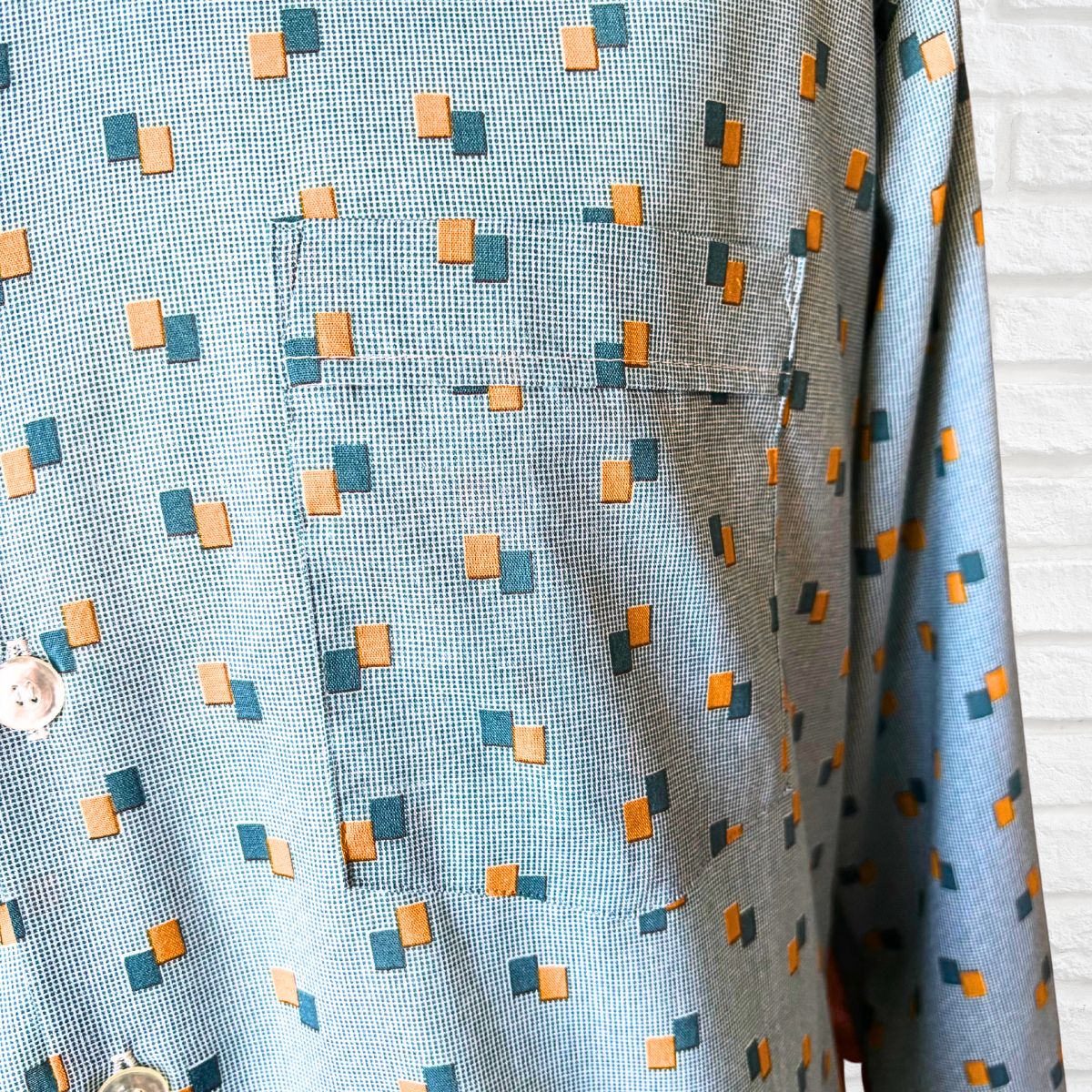 Close-up of a patterned fabric with small squares in blue, orange, and green on a light blue background.