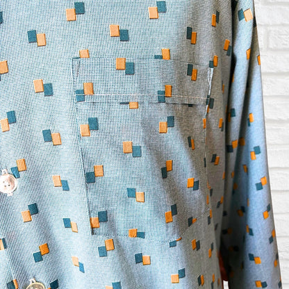 Close-up of a patterned fabric with small squares in blue, orange, and green on a light blue background.