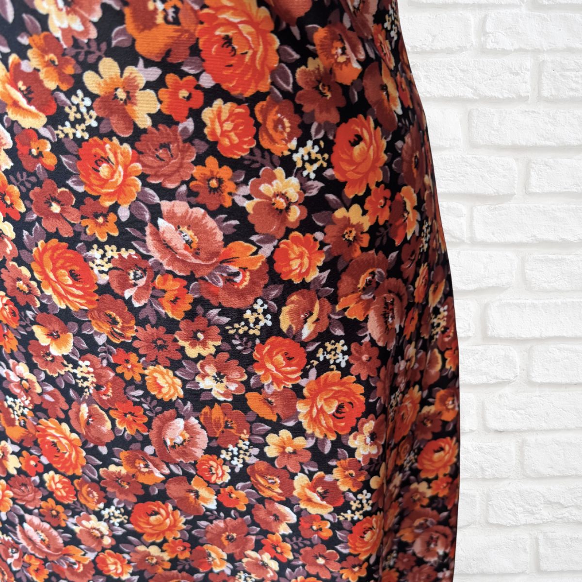 Close-up of a floral patterned fabric of a vintage dress against a white brick wall.