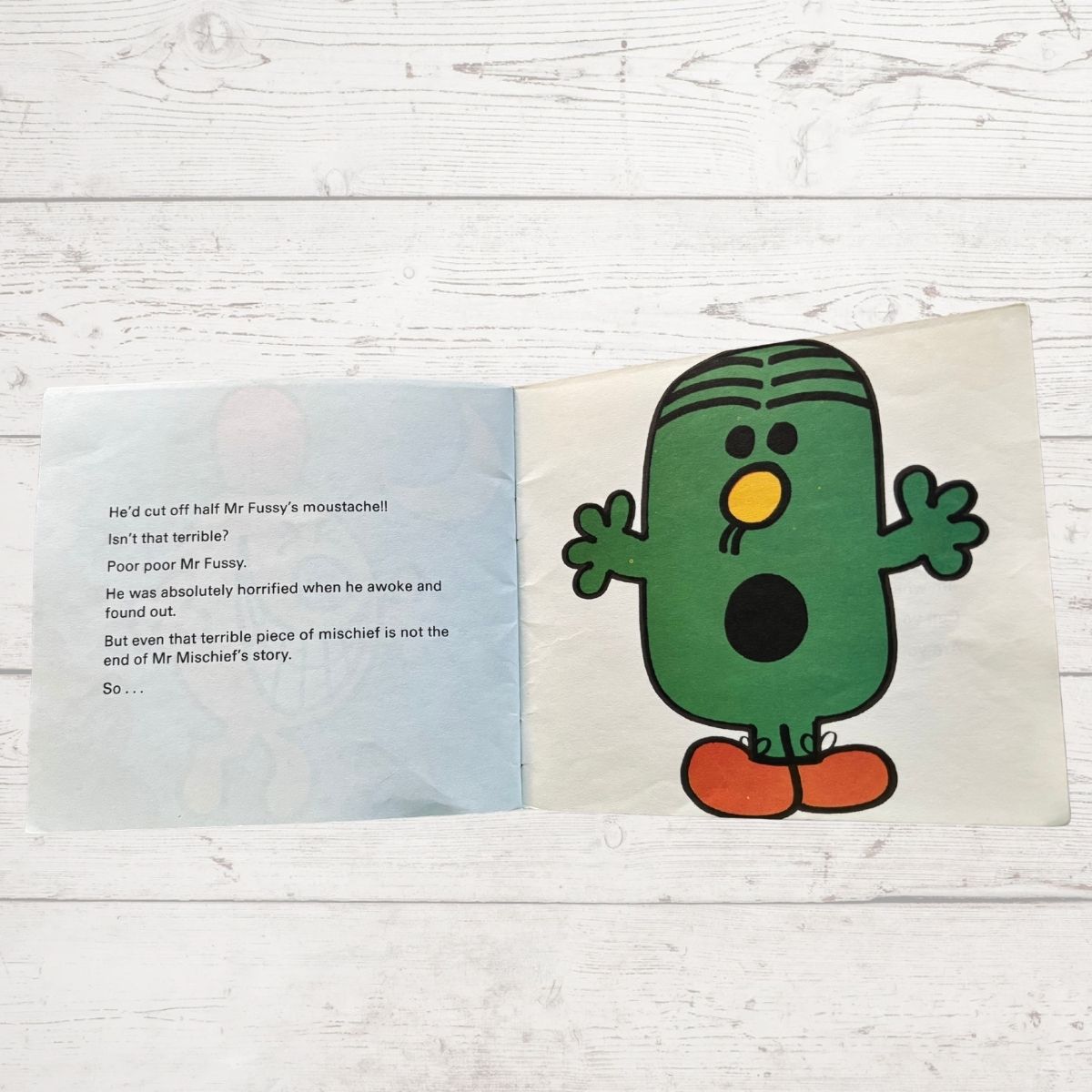 Open book with a green character Mr Fussy on a wooden surface
