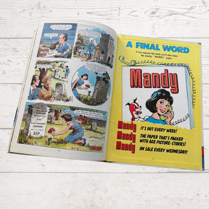 Comic book open to a page with 'Mandy' comic strip and promotional text on a wooden surface.