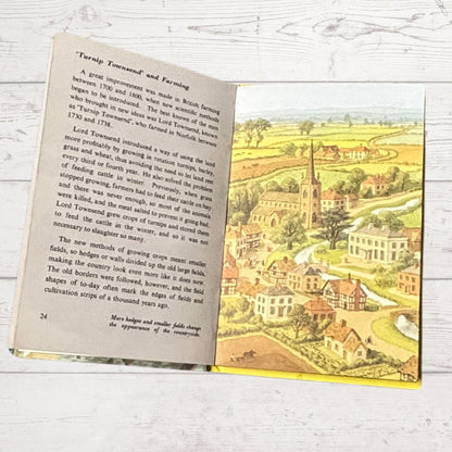 Open book with text and a colorful illustration of a village on a wooden surface