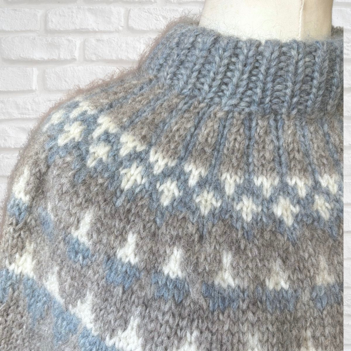 Knitted sweater with a pattern against a white brick wall