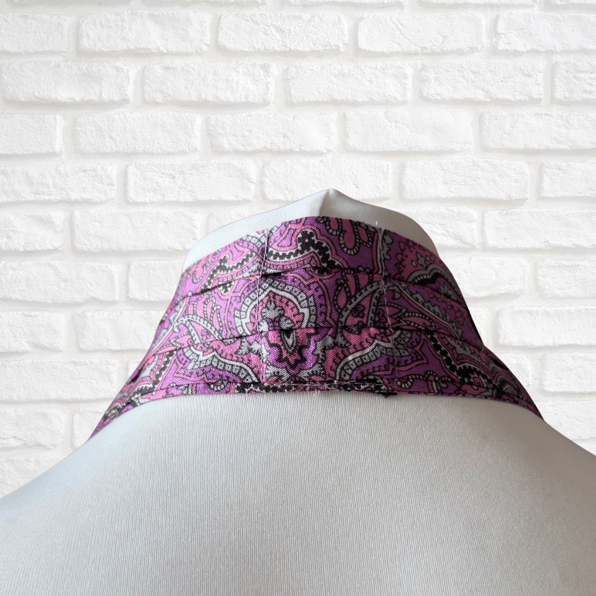 Purple paisley patterned cravat on a mannequin against a white brick wall.
