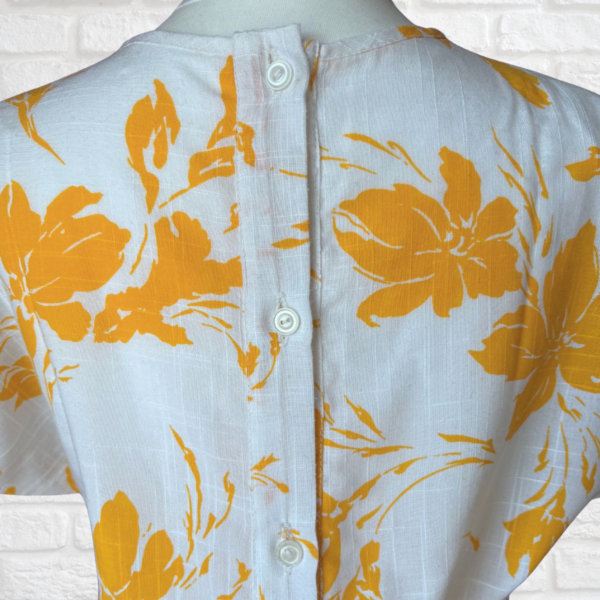 Mannequin wearing a white dress with large yellow floral patterns on a white background