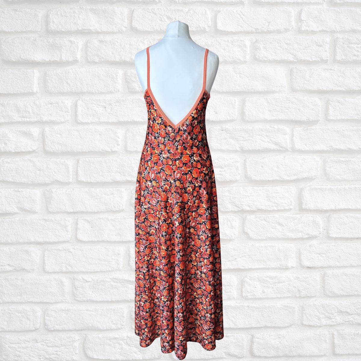 Black and orange floral  dress on a mannequin against a white brick wall
