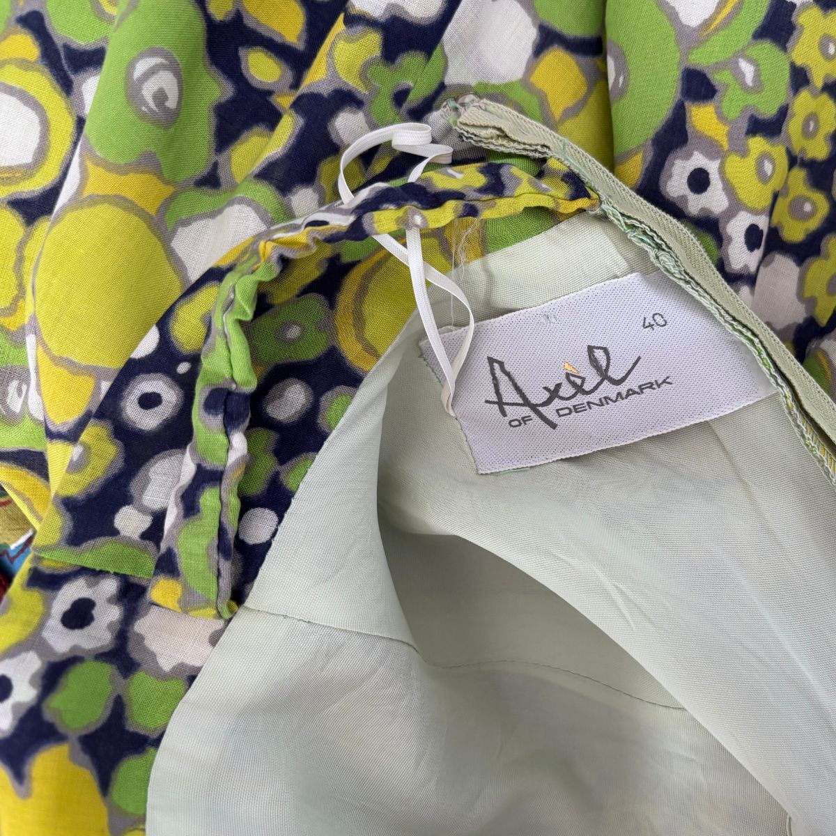 Close-up of a garment with a 'Axel of Denmark' tag, featuring colorful patterns in the background.