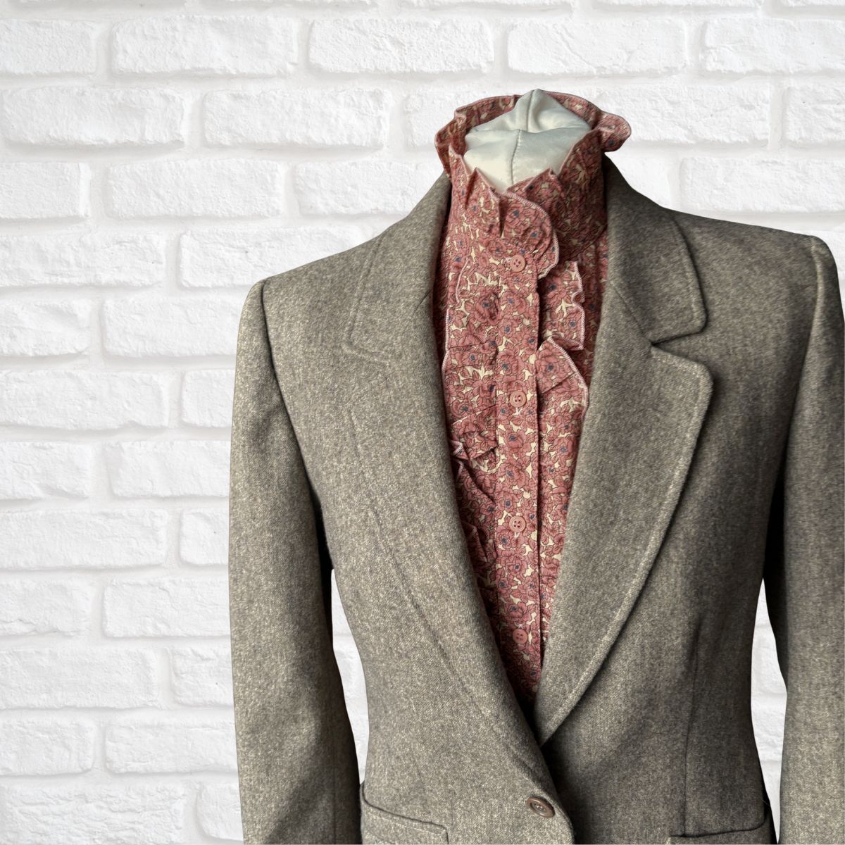 Warm neutral blazer with a patterned shirt against a white brick wall background