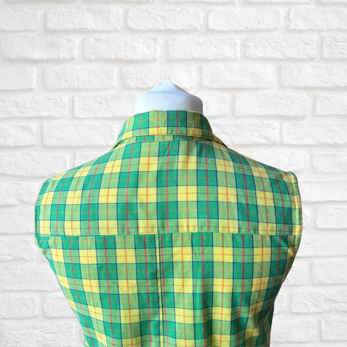 Green and yellow plaid shirt on a mannequin against a white brick wall background