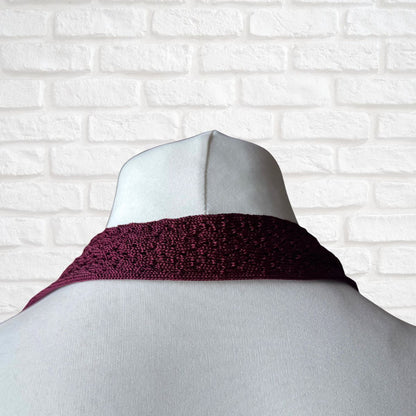Mannequin wearing a dark berry knitted tie against a white brick wall.